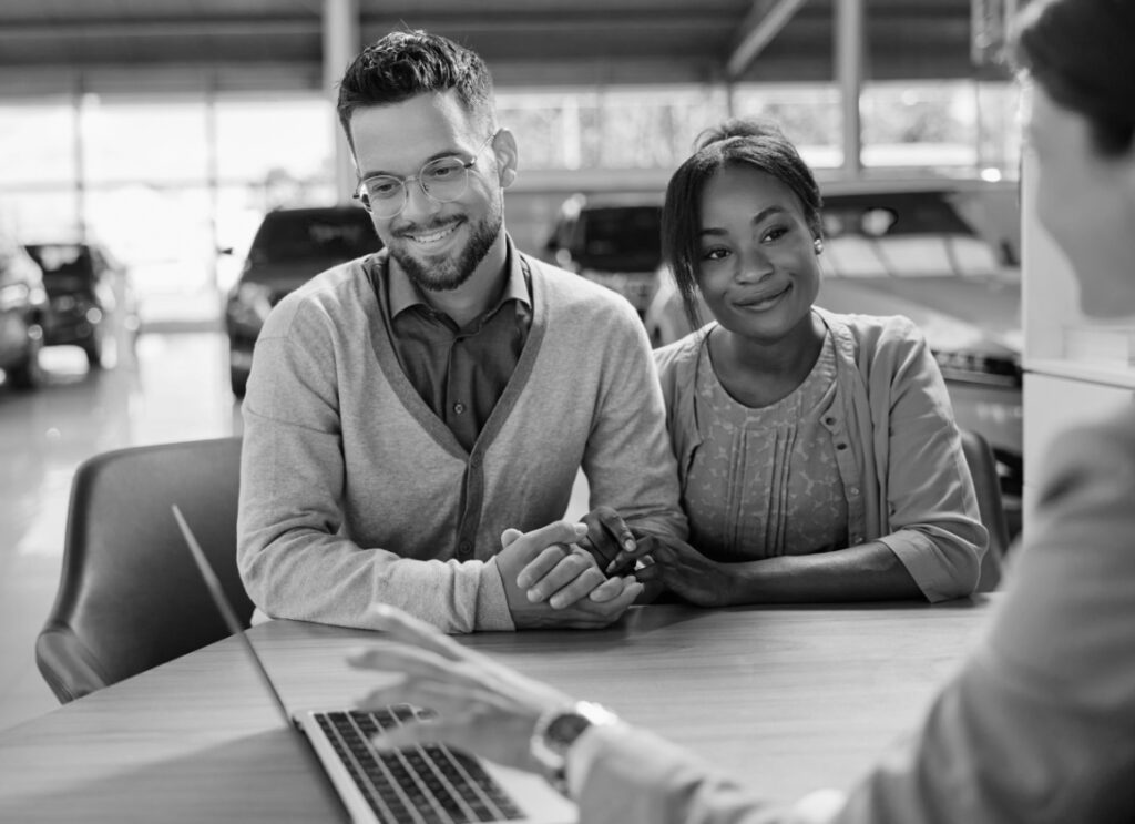 A married couple sit with a salesperson at a car dealership