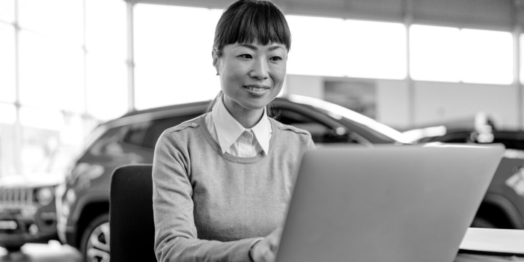 Woman typing on a laptop in an auto dealership representing the digital financing experience customers and dealers can expect when using CUDL.
