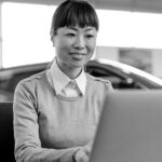 Woman typing on a laptop in an auto dealership representing the digital financing experience customers and dealers can expect when using CUDL.
